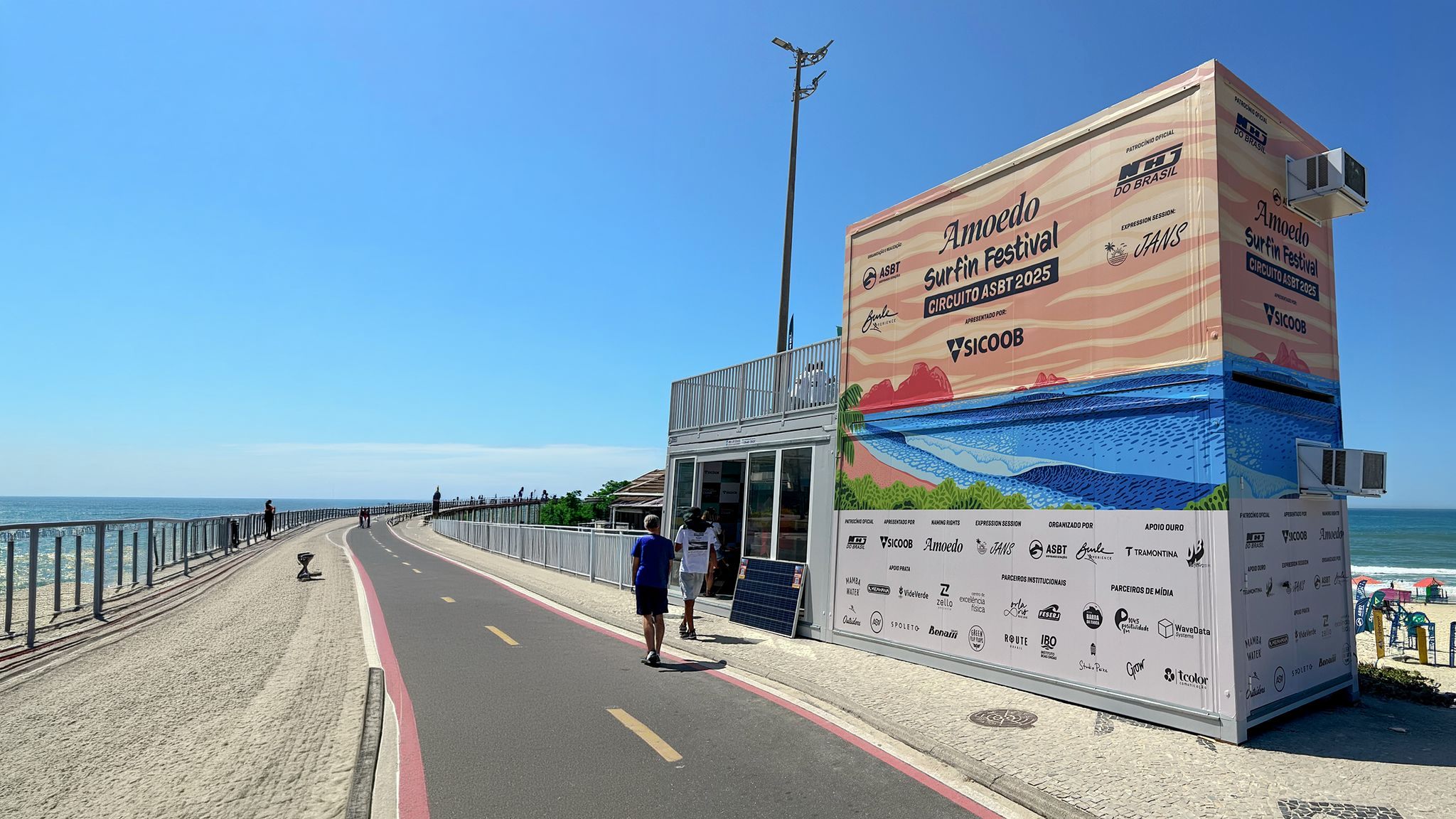 Contêiner do Amoedo Surf Fin Festival envelopado na orla, com a grade de patrocinadores na base